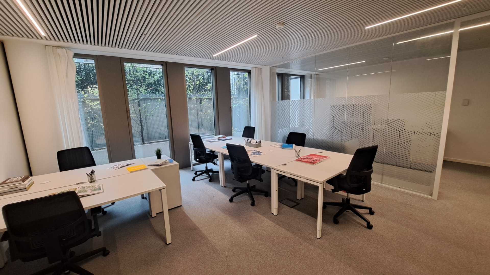 Bureau privé lumineux pour une équipe : bureaux blancs, chaises noires, grandes fenêtres et cloison vitrée